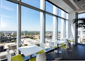 Thumbnail 15 of 18 - A room with white tables and chairs with a view of the city outside the windows.