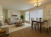 Thumbnail 2 of 8 - A well-lit living room with a grey couch, a wooden coffee table, and a dining table with chairs.