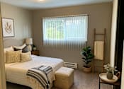Thumbnail 1 of 8 - A bedroom with a bed, a chair, a potted plant, and a window with blinds.