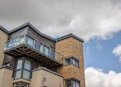 Thumbnail 1 of 7 - the side of a brick building with a balcony and a cloudy sky