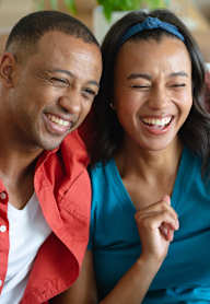 A man and a woman are laughing while looking at a tablet.