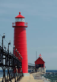 A red lighthouse stands tall on a pier over the ocean.