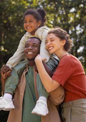 A man is carrying a child on his shoulders while standing in a wooded area at Peach Tree Apartments, Iowa, 50021