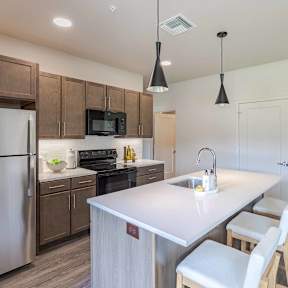 A kitchen with a refrigerator, microwave, oven, sink, and cabinets.