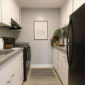 A black refrigerator sits in a kitchen with white cabinets and a grey counter.