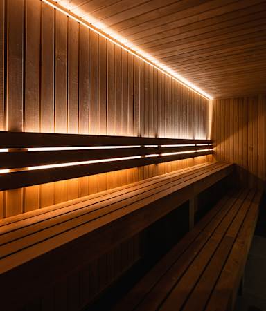 A sauna with wooden benches and walls, illuminated by a row of lights.
