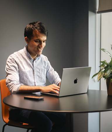 A man is sitting at a table using a laptop.