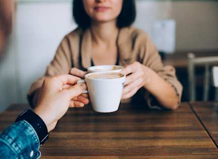 A person is holding a cup of coffee in front of another person.