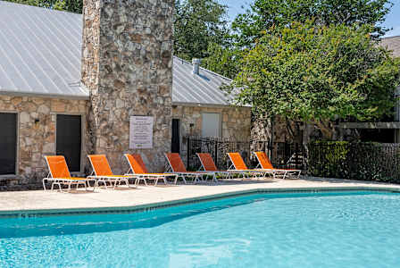 A pool with chairs and a stone pillar in front of a building.