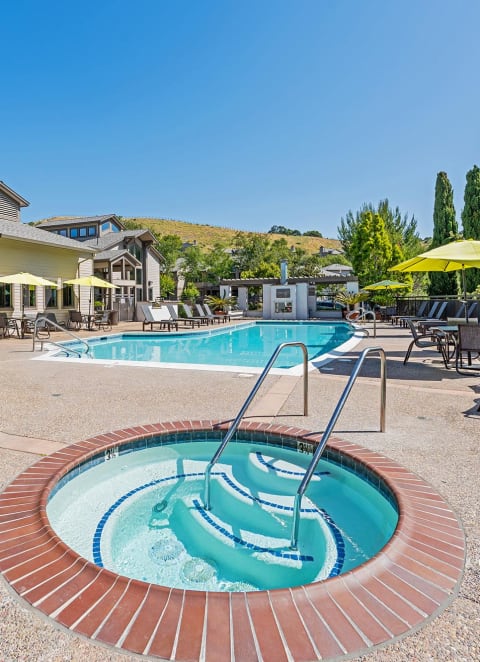 a swimming pool with a hot tub and a patio with chairs and umbrellas