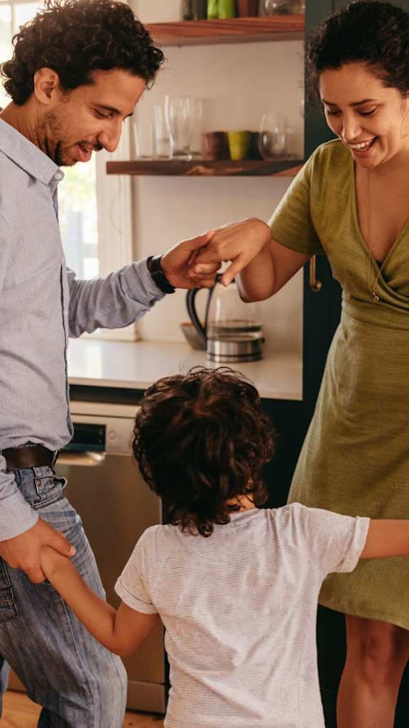 A family of three are dancing together in their kitchen.