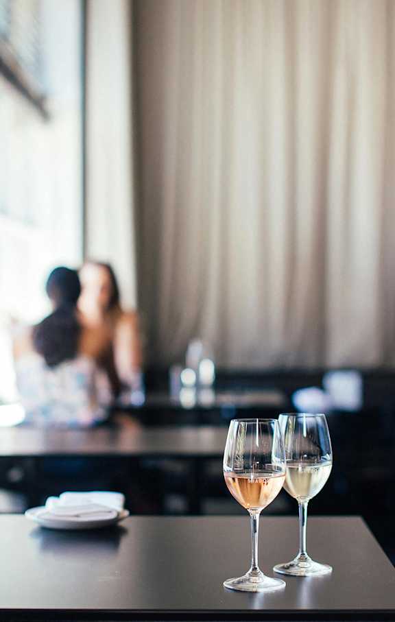 Two glasses of wine are on a table in a brightly lit room.