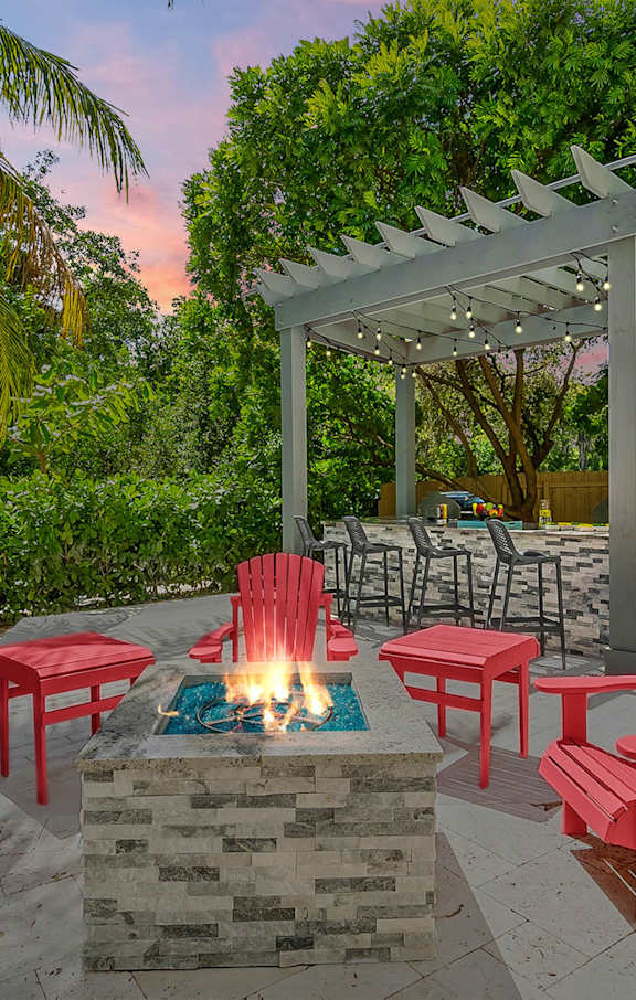 a fire pit with red chairs and a white pergola in the background