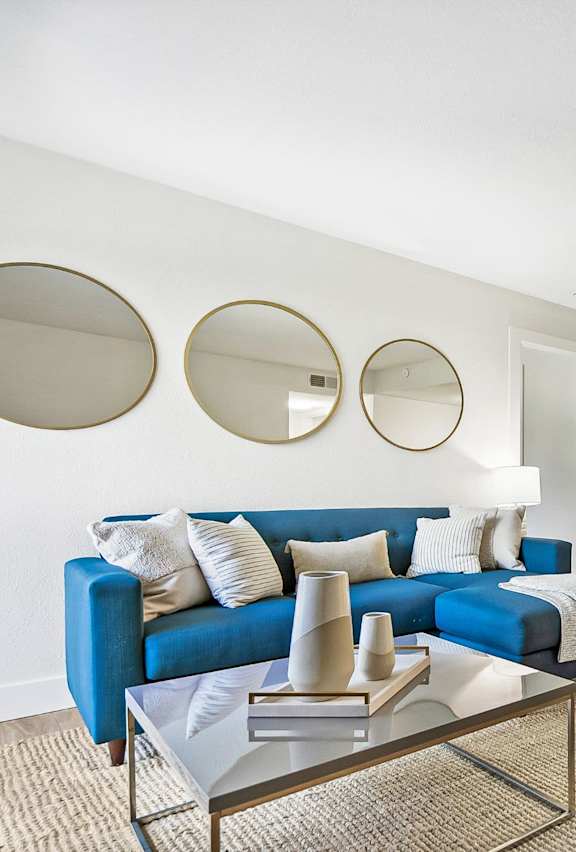 A living room with a blue couch and a glass coffee table.