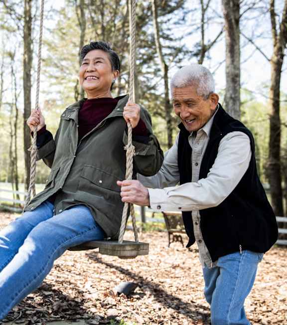 an older man and woman playing on a swing in a park