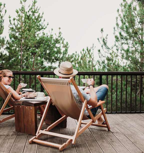 Two people are sitting in deck chairs on a wooden deck.