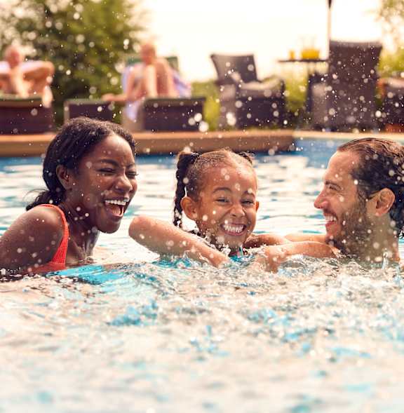 Three people are splashing in a pool.