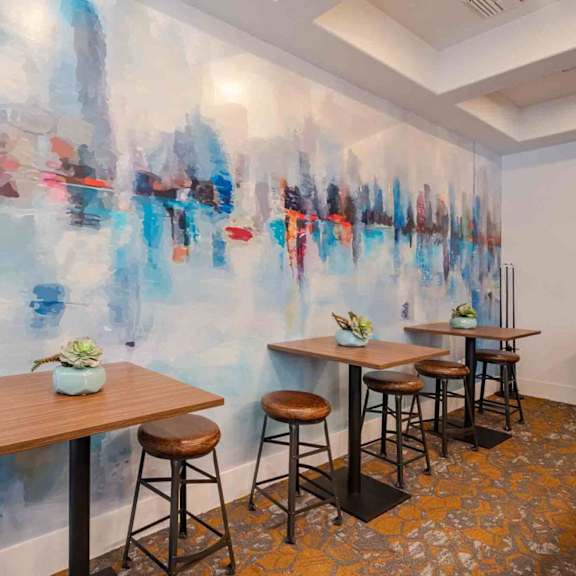 A room with a wall mural and a table with four stools.