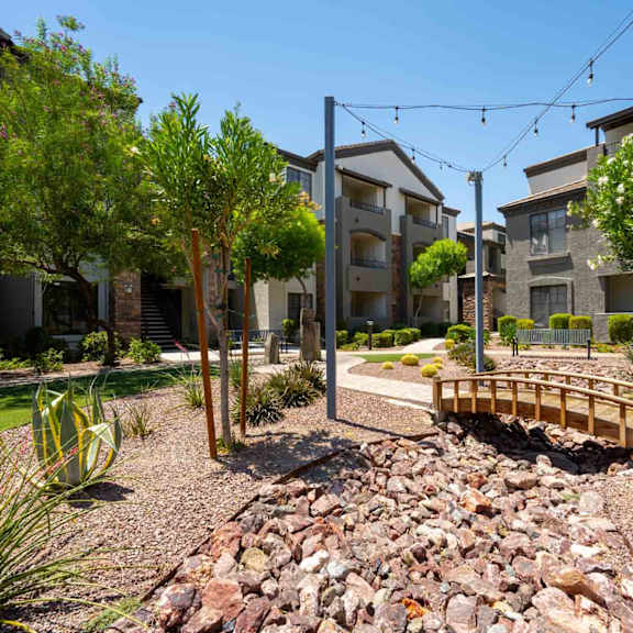 A small bridge crosses a rocky area in front of apartment buildings.