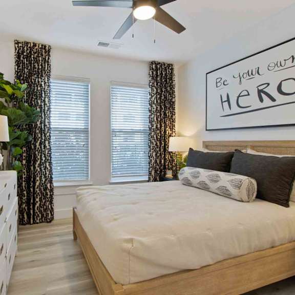 A bedroom with a bed, dresser, mirror, and a sign that says "Be Your Own HERO.".