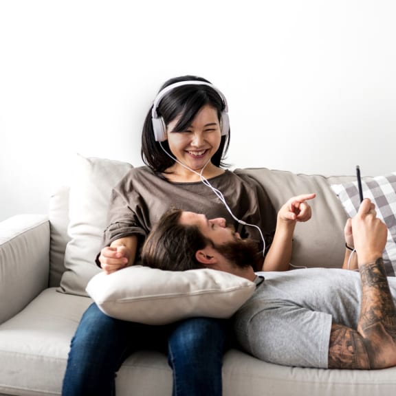 Man and a woman sitting on a couch wearing headphones and looking at a tablet