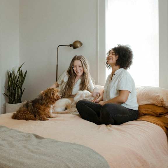 Two women sitting on a bed with a dog.