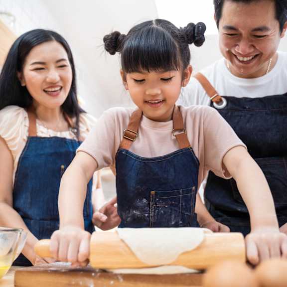 A woman and a girl are rolling out dough on a kitchen counter.