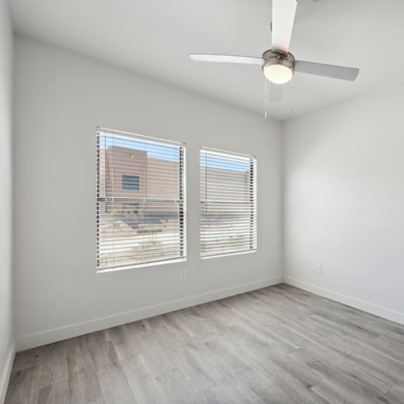 A room with a ceiling fan and two windows.