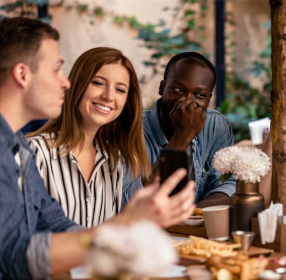 a group of people sitting around a table talking and looking at a cell phone