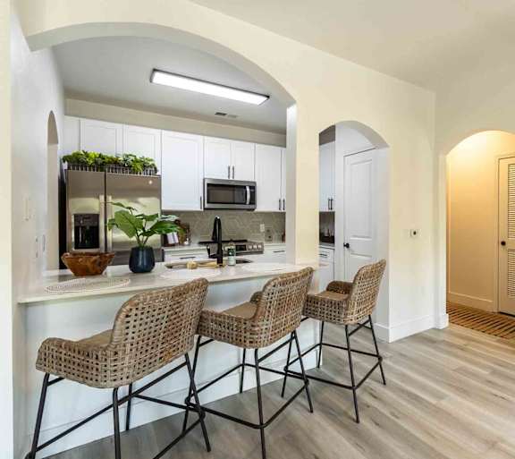 A kitchen with white cabinets and a white countertop with a refrigerator, microwave, and sink.