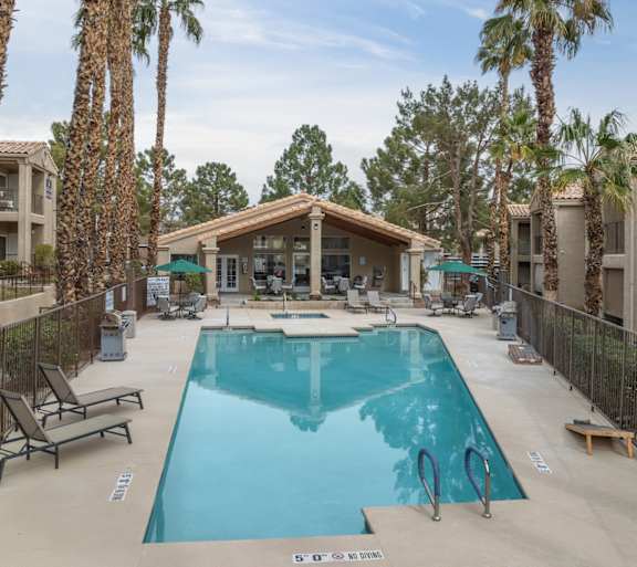 A swimming pool surrounded by palm trees and a building in the background.