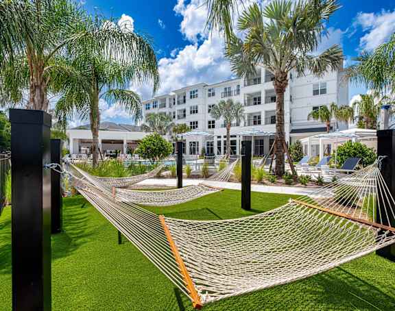 A large white building with a glass entrance and two palm trees in front. at Altis Twin Lakes Apartments, Kissimmee, FL 34744