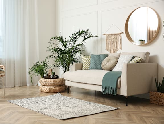 A living room with a beige sofa, a round mirror, and a woven basket on the floor.
