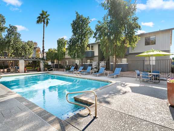 A pool surrounded by chairs and trees.