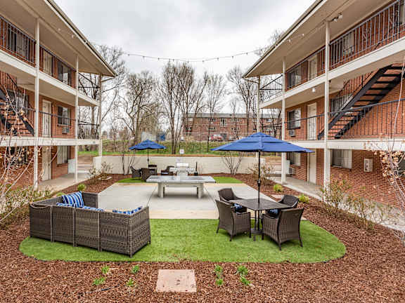 A courtyard with a table, chairs and umbrellas surrounded by buildings.