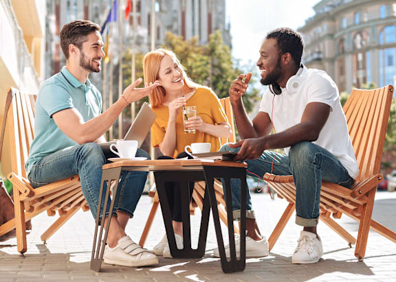 Three friends are sitting at a table outside, enjoying a conversation and drinks.