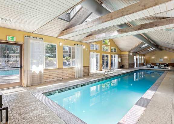 A large indoor swimming pool with a wooden ceiling and a glass door leading outside.
