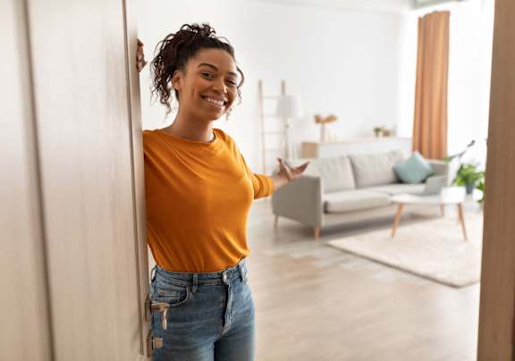A woman in a yellow top and blue jeans stands in a room with a couch and a rug.