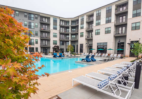 a swimming pool with lounge chairs in front of an apartment building