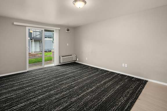 A room with a black carpet and a sliding glass door leading to a balcony.