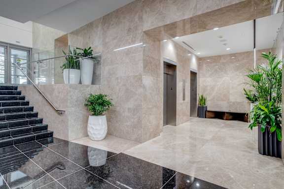 A hallway with marble floors and walls, a staircase, and potted plants.