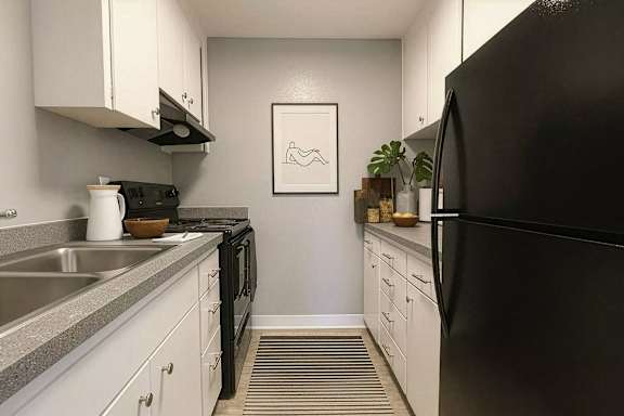 A black refrigerator sits in a kitchen with white cabinets and a grey counter.
