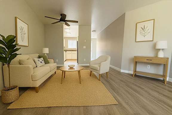 A living room with a beige couch, a coffee table, a ceiling fan, and a plant.