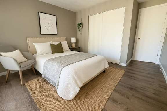 A bedroom with a bed, chair, and a rug.