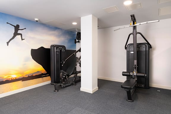 a gym with two exercise machines and a wall mural of a running woman at The Trilogy Apartments, Manchester, M15 4RU