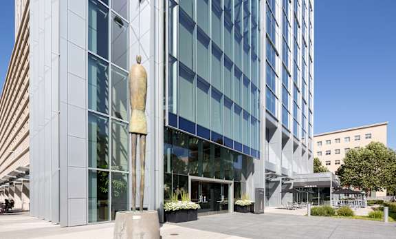 A large building with a glass facade and a tall sculpture in front.