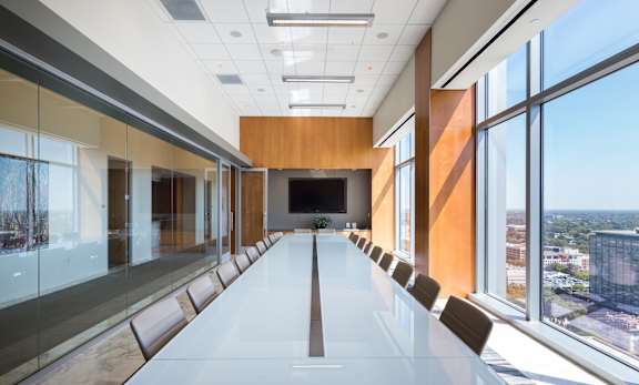 A long white table is in a conference room with a view of the city.