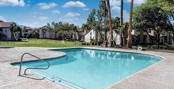 A pool surrounded by palm trees and a building.