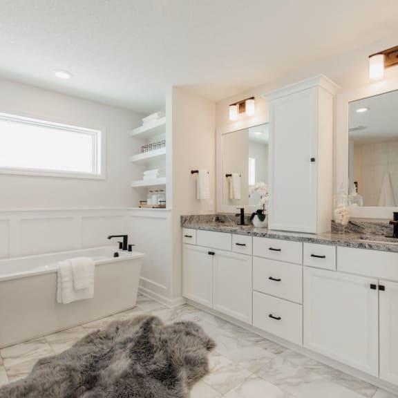 a bathroom with white cabinets and a bath tub and a sink and a mirror