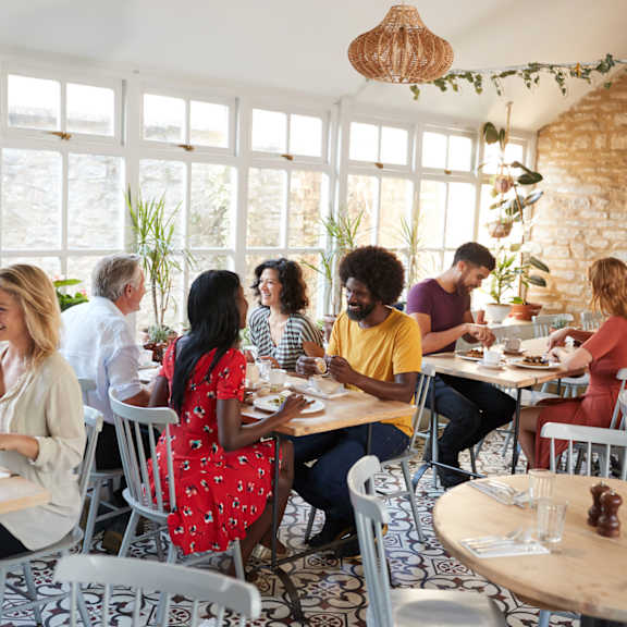 A group of people are sitting at tables in a restaurant with a brick wall in the background.